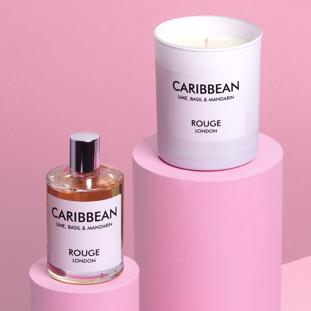 A gift set by Rouge London including a white candle in a container and a spray bottle, both labeled 'Caribbean - Lime, Basil & Mandarin'. The items are presented in a white box with a black ribbon.