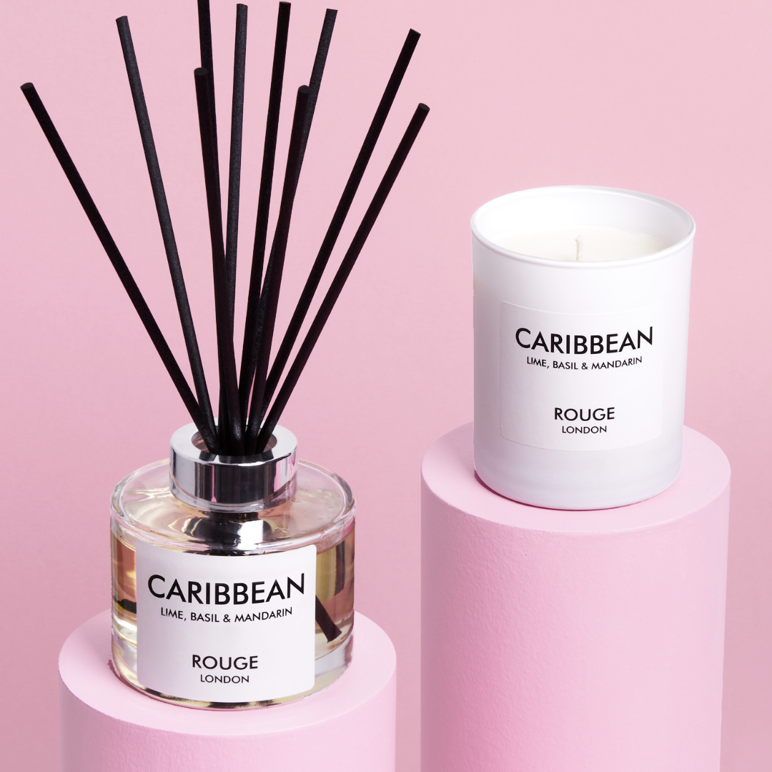 A luxury candle and diffuser gift collection with the label 'Caribbean - Lime, Basil & Mandarin' by Rouge London. The candle is white, and the diffuser is clear with black reed sticks.